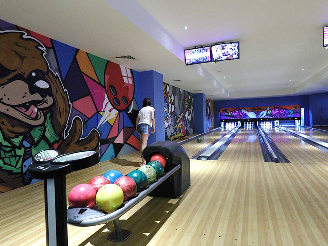 Bowlinghalle im Sueno Hotels Deluxe Belek mit bunten Wänden und einer Frau, die eine Kugel vorbereitet.