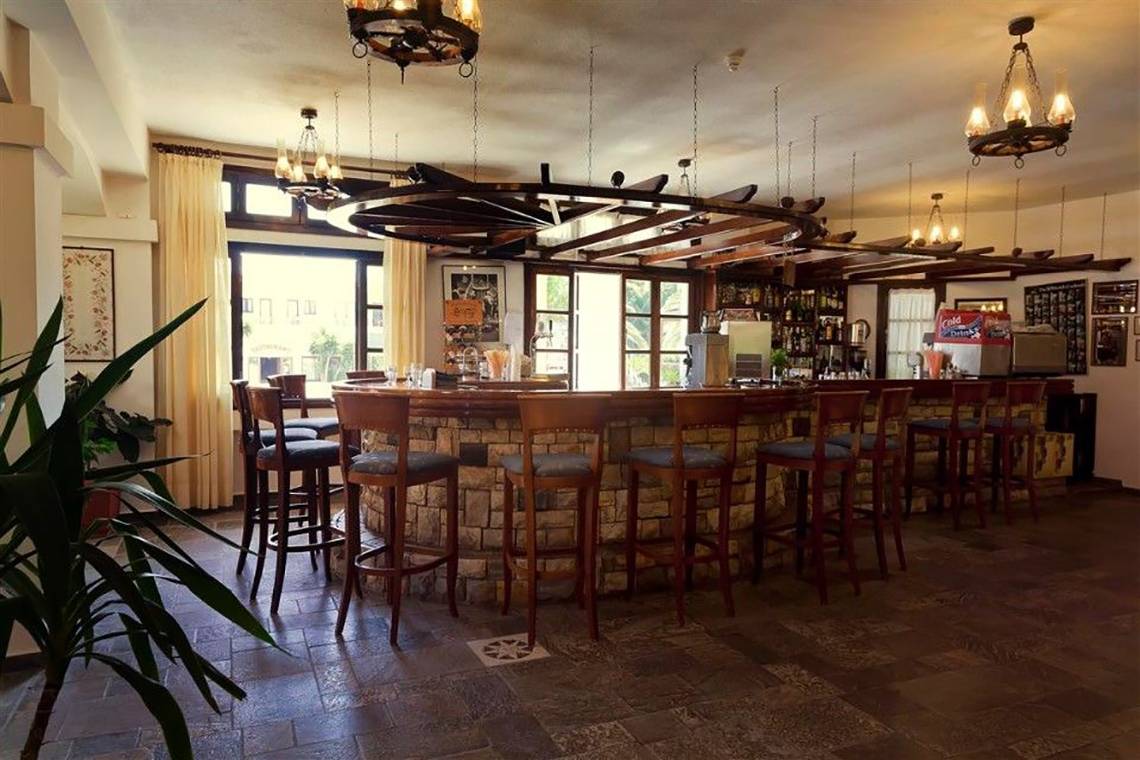 Innenansicht der Bar im Atlantica Marmari Beach Hotel mit Steinmauer und Holzbarhockern.