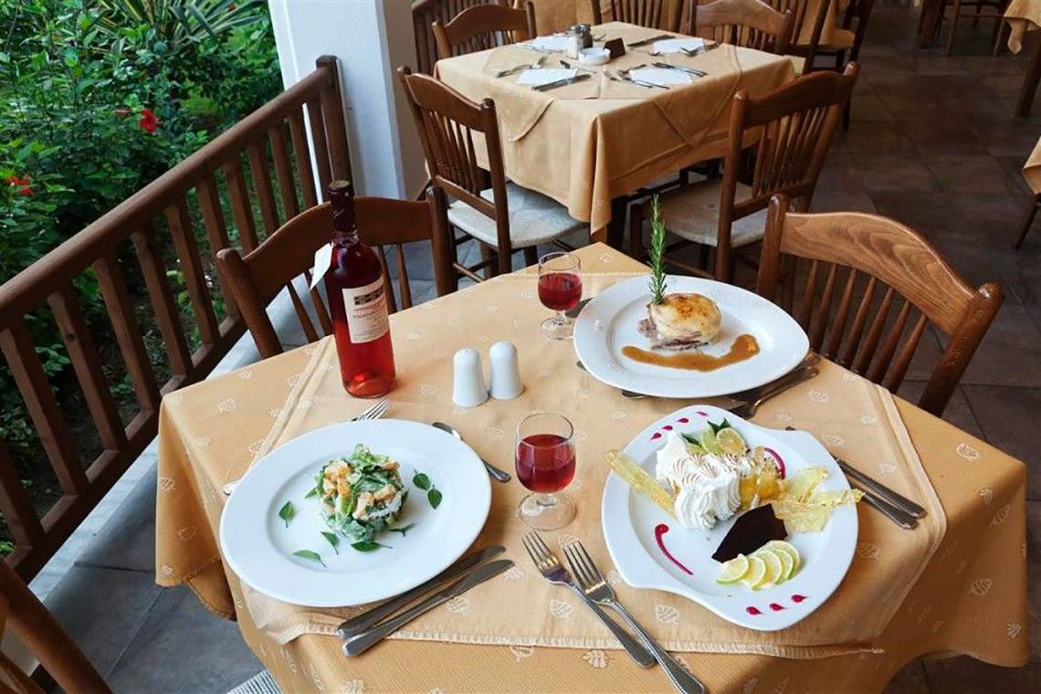 Tisch im Restaurant des Atlantica Marmari Beach Hotel mit Tellern, Wein und Dekoration.