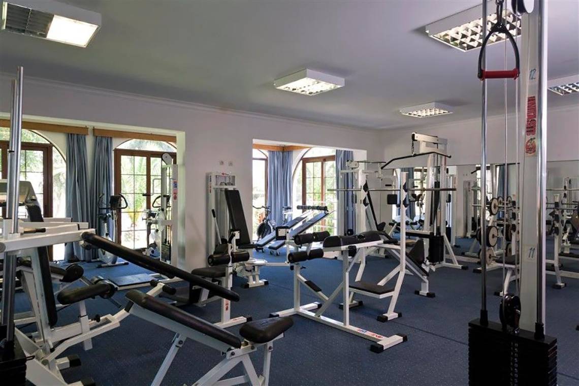 Fitnessstudio im Atlantica Marmari Beach Hotel mit verschiedenen Geräten und blauem Boden.