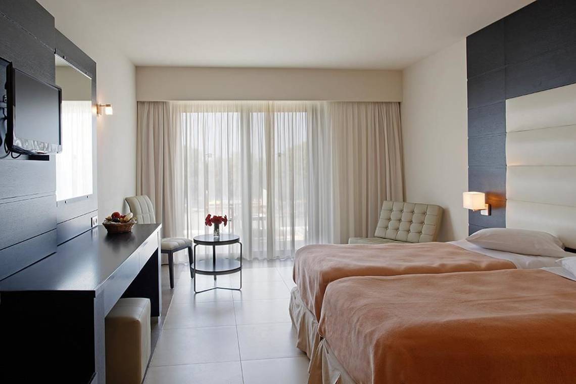 Doppelzimmer im Atlantica Holiday Village Kos mit zwei Betten, Fernseher, Tisch und Stühlen.