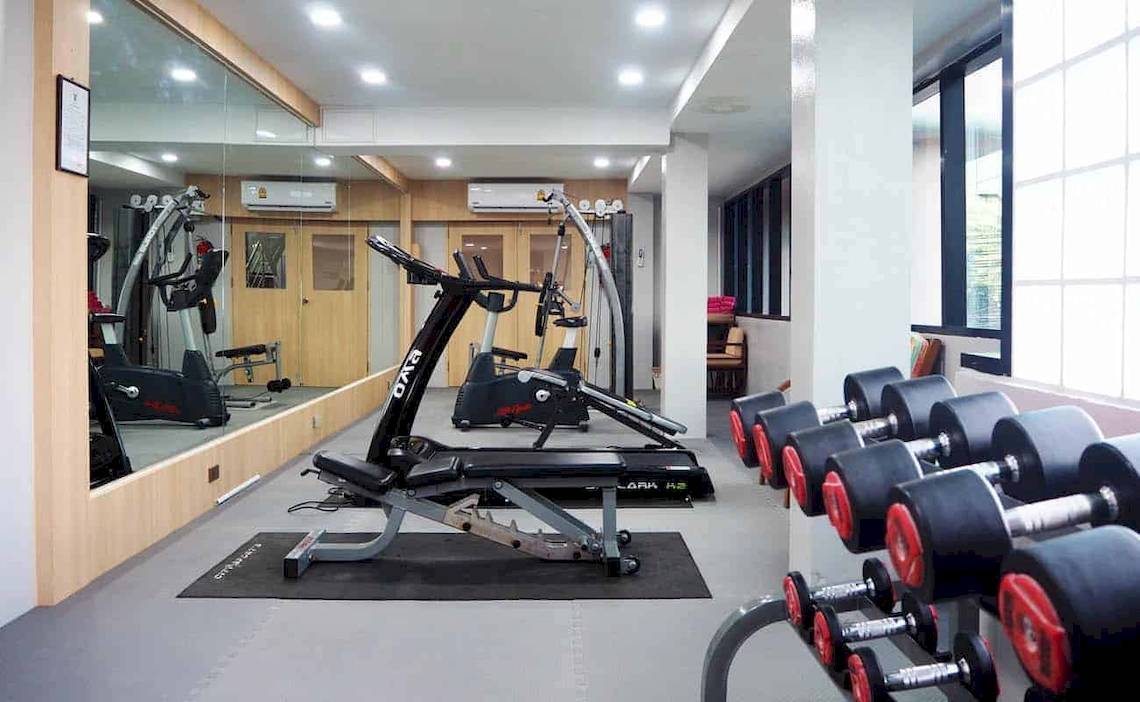 Fitness-Center im Chaba Samui Resort mit Laufbändern, Hanteln und einer Glaswand.