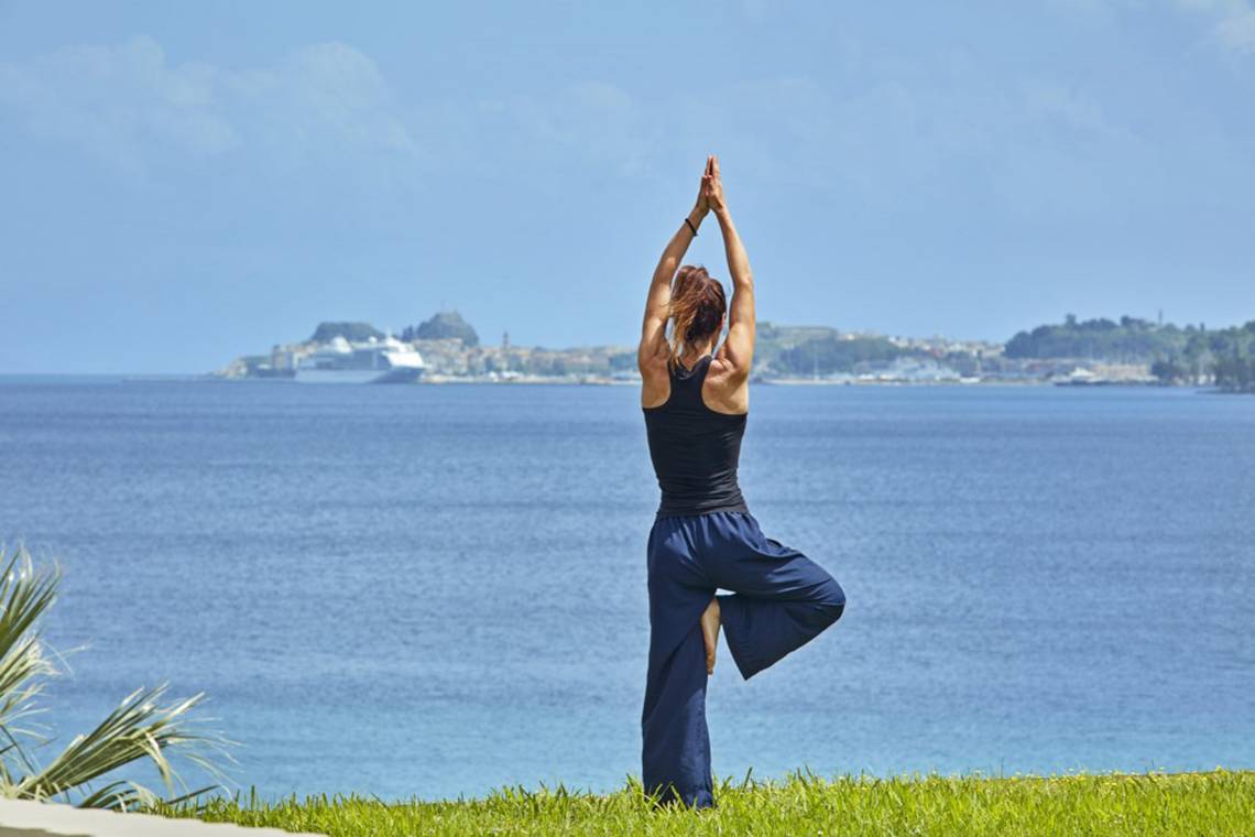 Eine Frau praktiziert Yoga auf einem Grashang mit Blick auf das Meer.
