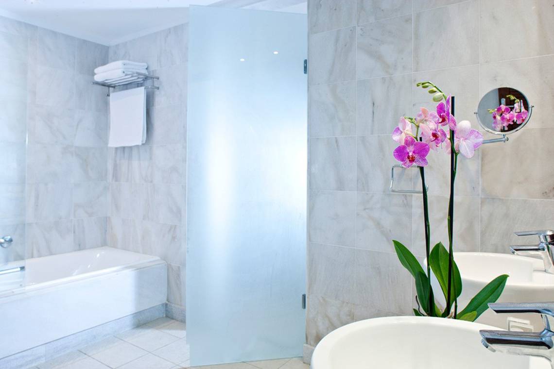 Badezimmer im Kontokali Bay Resort & Spa mit Badewanne, Waschbecken und Orchideenstrauß.