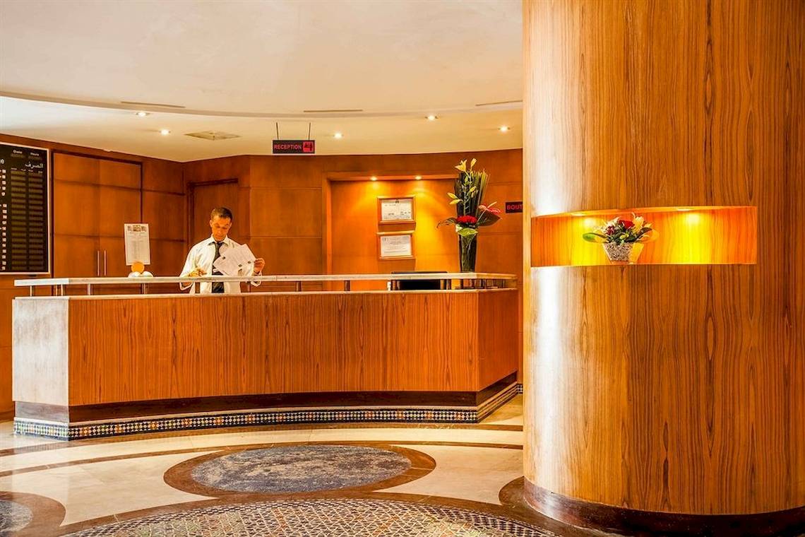 Rezeption im Allegro Agadir Hotel mit Angestelltem und Blumendekoration.