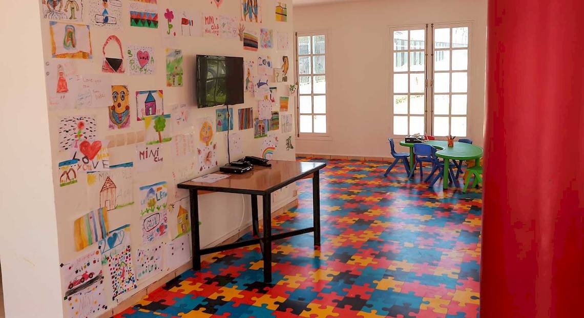 Spielzimmer im Allegro Agadir Hotel mit buntem Puzzleboden, Fernseher an der Wand, Schreibtisch und bunten Stühlen.