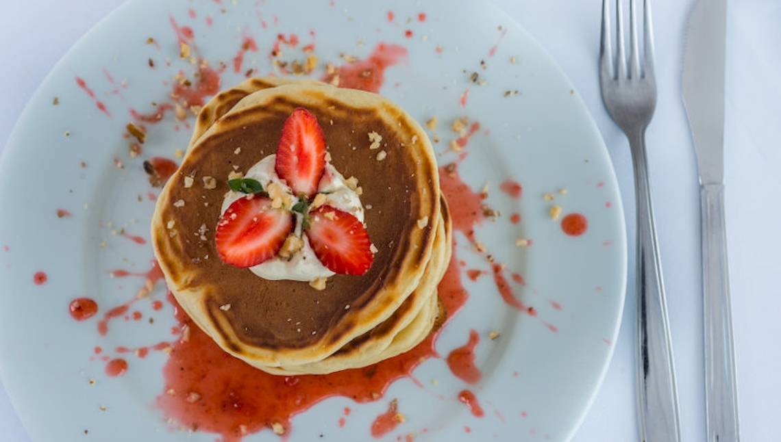 Ein Dessertteller mit zwei Stapeln von Pfannkuchen, überzogen mit Erdbeeren, Sahne und Beerensauce.