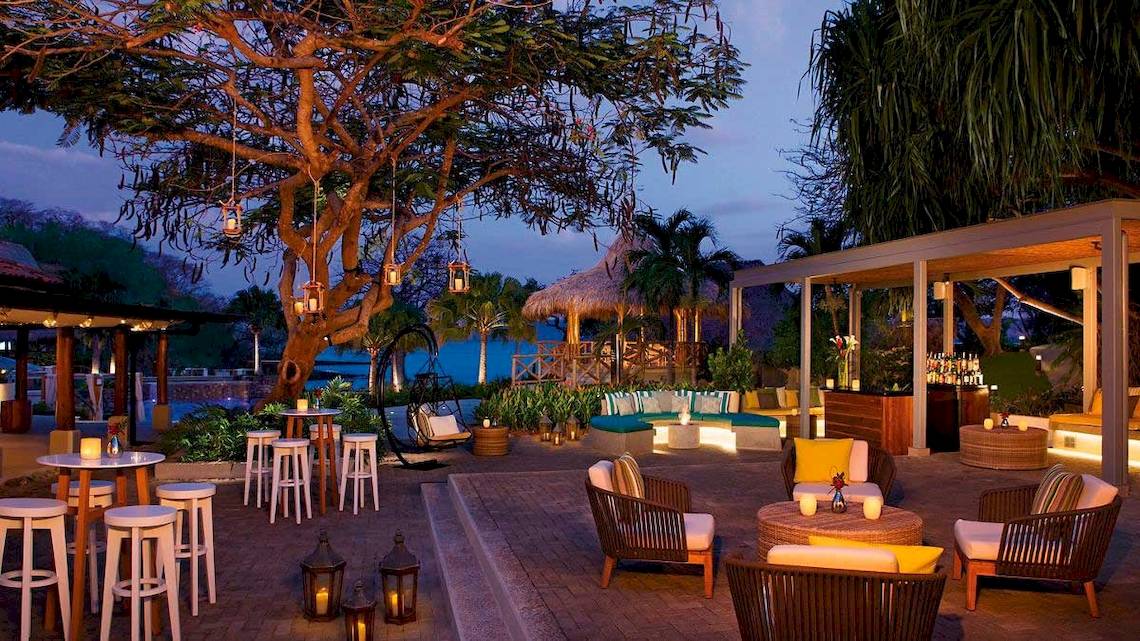 Außenbereich des Secrets Papagayo Costa Rica Hotels mit Beleuchtung, Möbeln und Blick auf den Ozean.