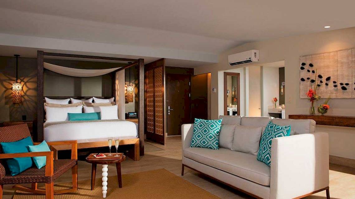 Schlafzimmer im Secrets Papagayo Costa Rica mit einem Bett, Kissen und einem Wohnzimmerbereich.