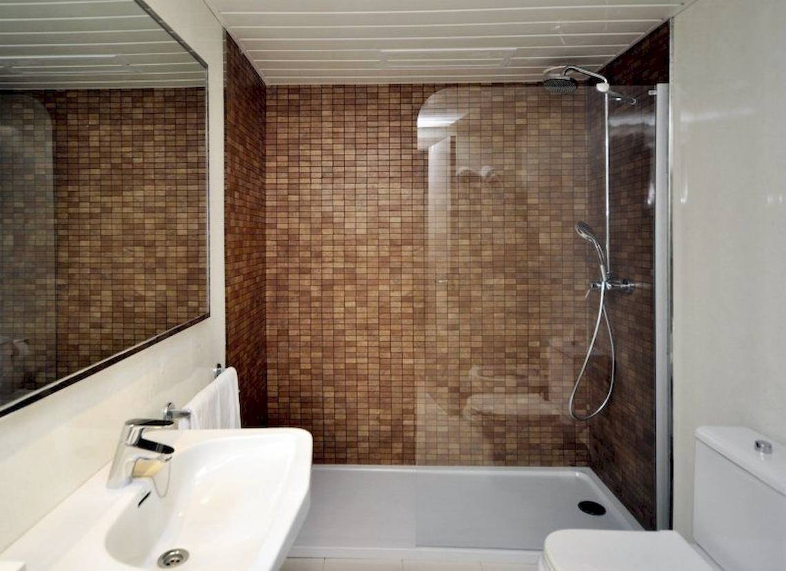 Badezimmer mit braunen Fliesen, Dusche, Spiegel und Toilette im Sol Wave House All Suites Hotel