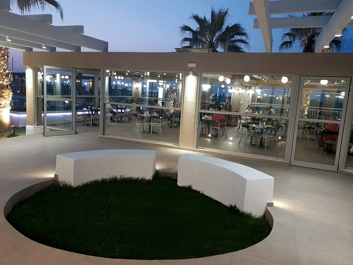 Außenterrasse des Europa Beach Hotel & Spa mit Gästen an Tischen und Palmen im Hintergrund.