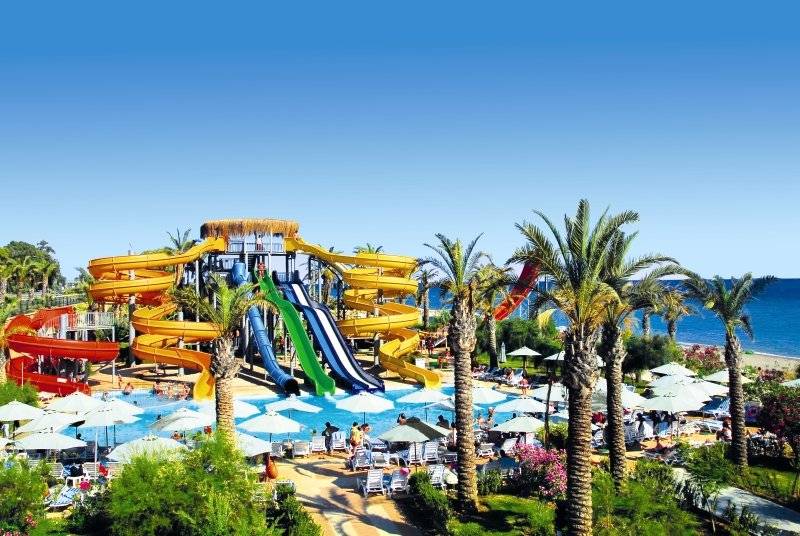 Wasserpark des Long Beach Alanya Hotels mit mehreren Rutschen und vielen Sonnenschirmen.