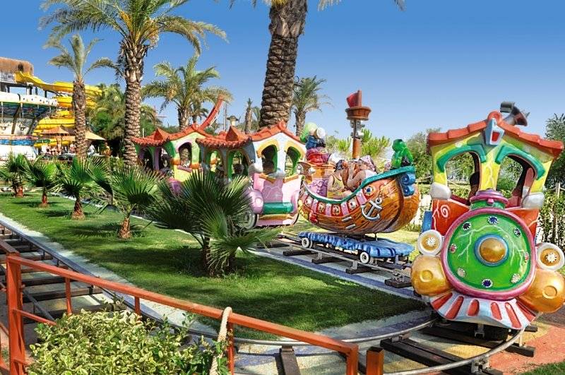 Kinderzug im Freizeitpark des Long Beach Alanya Hotels mit bunten Waggons und Palmen im Hintergrund.