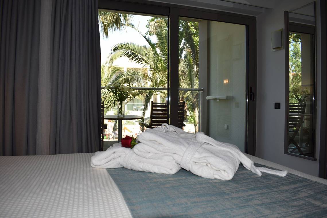 Ein Bett mit weißen Bademänteln und einer roten Rose auf einem Balkon im Minos Mare Hotel.