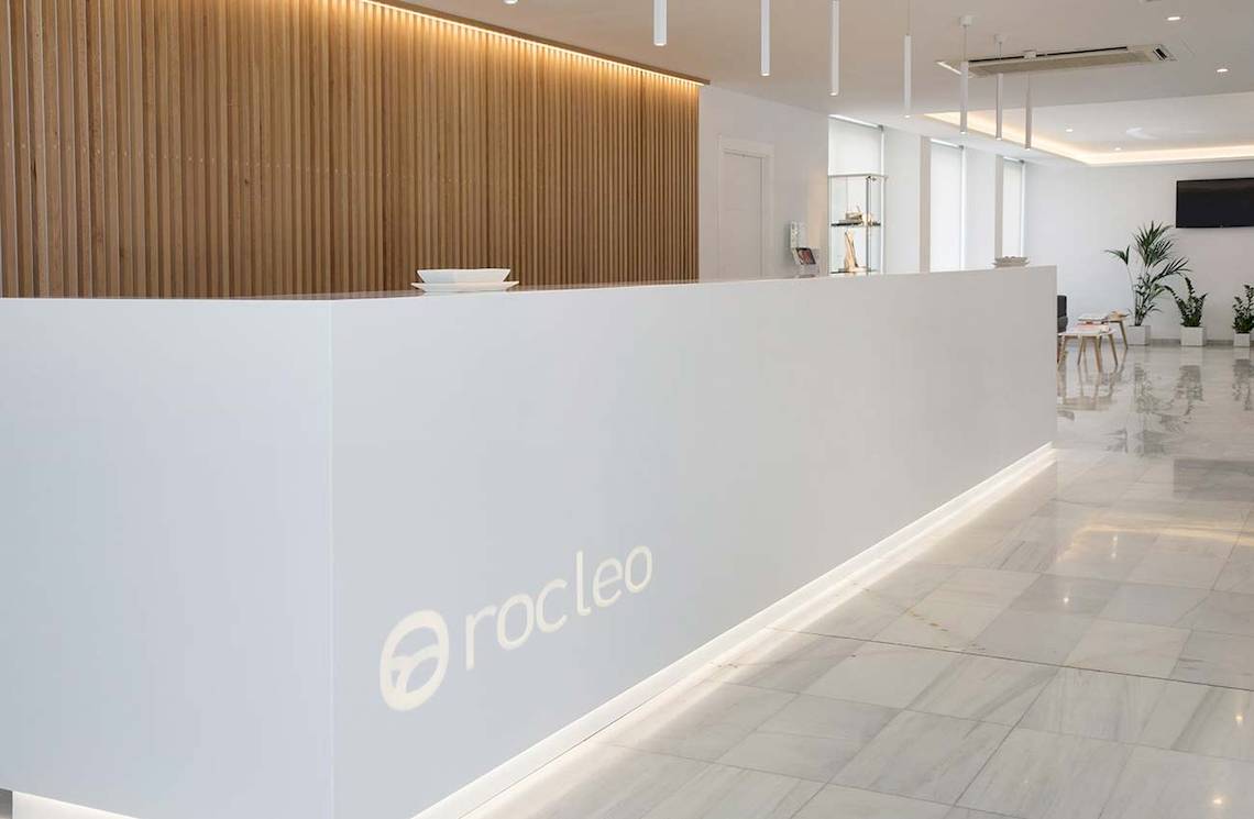 Empfangsbereich des Alua Leo Hotels mit moderner weißer Theke und Logo.