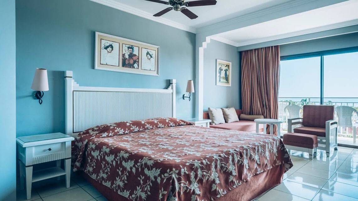 Ein Hotelzimmer im Iberostar Laguna Azul Hotel mit einem Bett, Nachttischen, Lampen und einem Balkon.