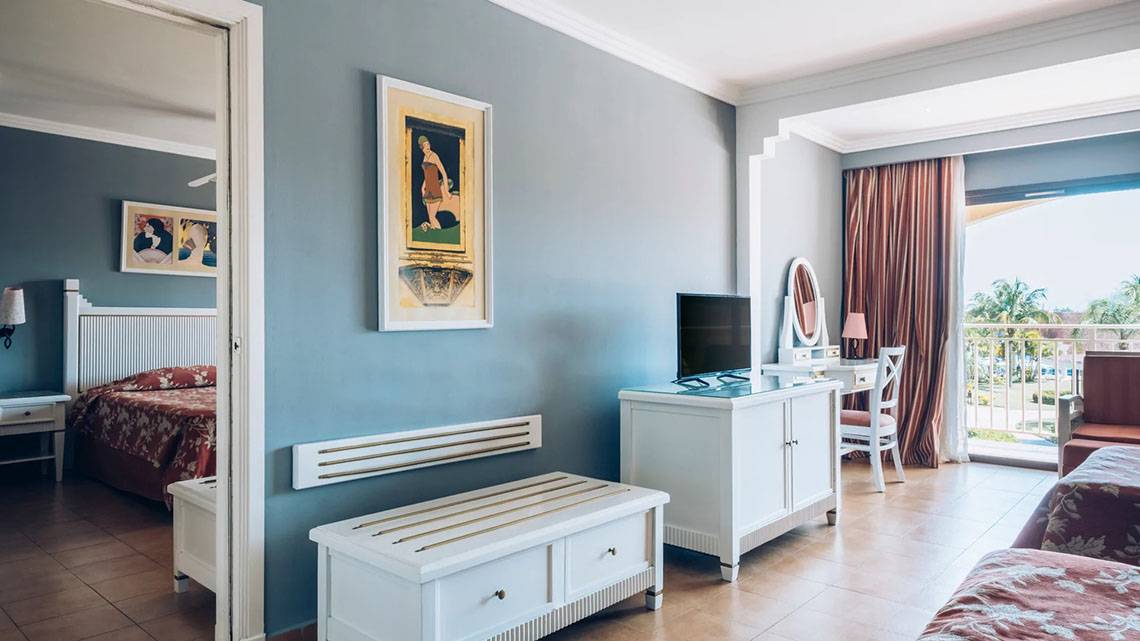 Innenansicht eines Hotelzimmers im Iberostar Laguna Azul, mit zwei Betten, Fernseher, Schreibtisch und Balkon.