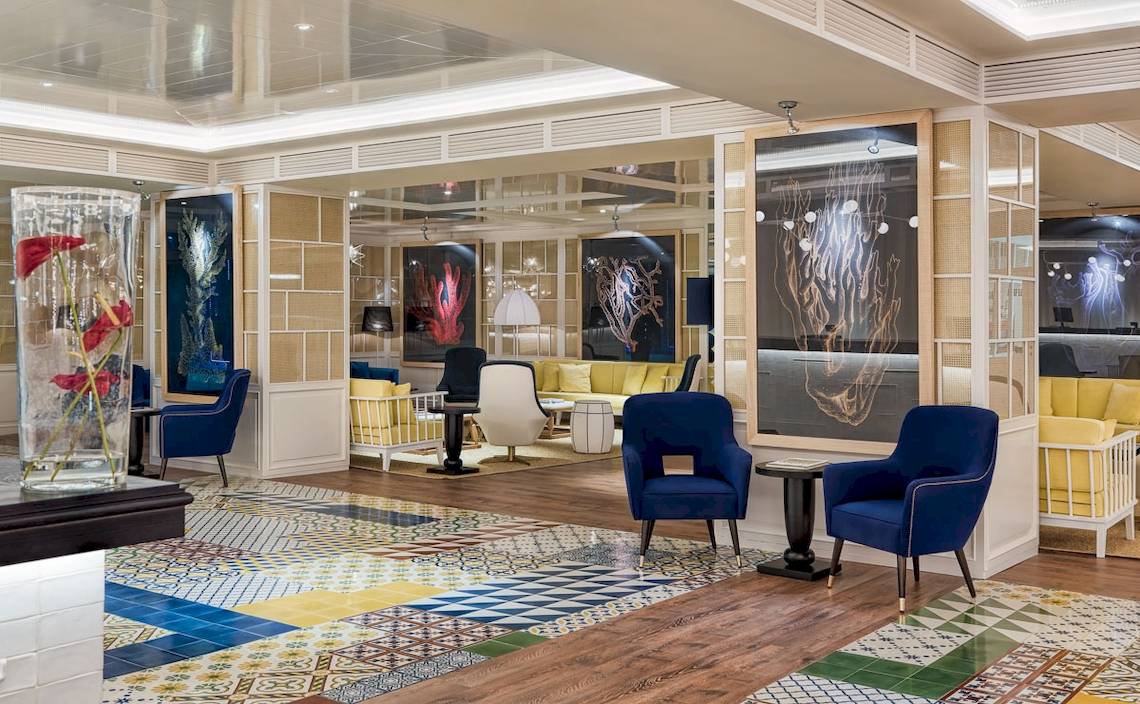 Lobby des H10 Las Palmeras Hotels mit blauen Stühlen und bunten Fliesen.