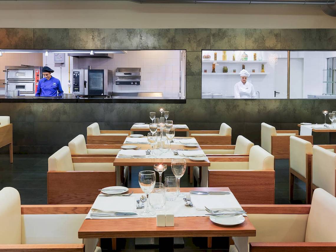 Innenansicht des Restaurants im H10 Las Palmeras Hotel mit gedeckten Tischen und Köchen, die im Hintergrund arbeiten.