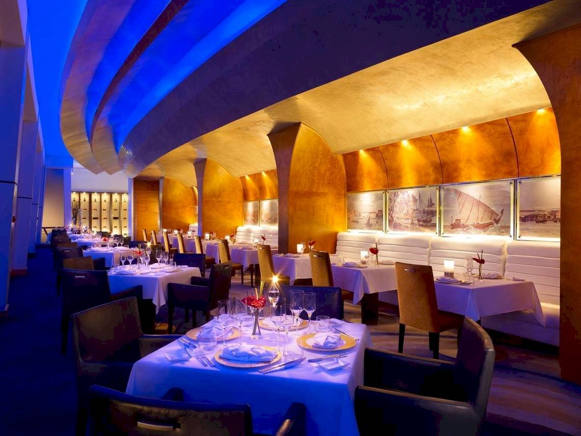 Innenansicht des Restaurants Shangri-La Barr Al Jissah Resort & Spa - Al Bandar mit blauer Beleuchtung und eingerichteten Tischen.