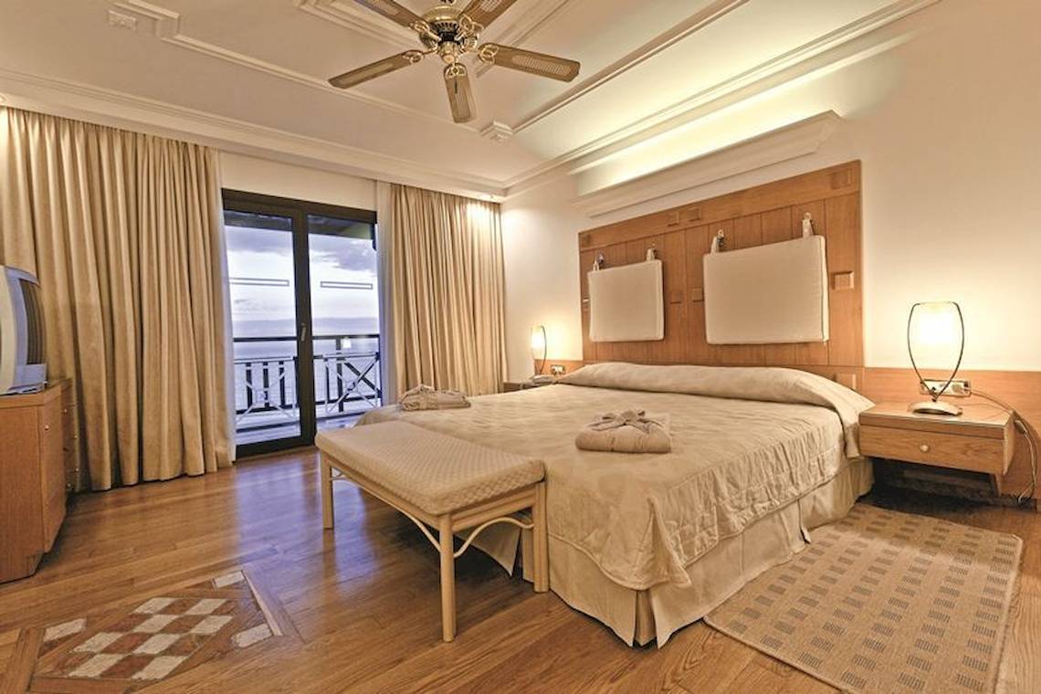 Schlafzimmer im Mitsis Royal Mare Thalasso & Spa Resort mit großem Bett, Balkon, Holzboden und modernen Möbeln.