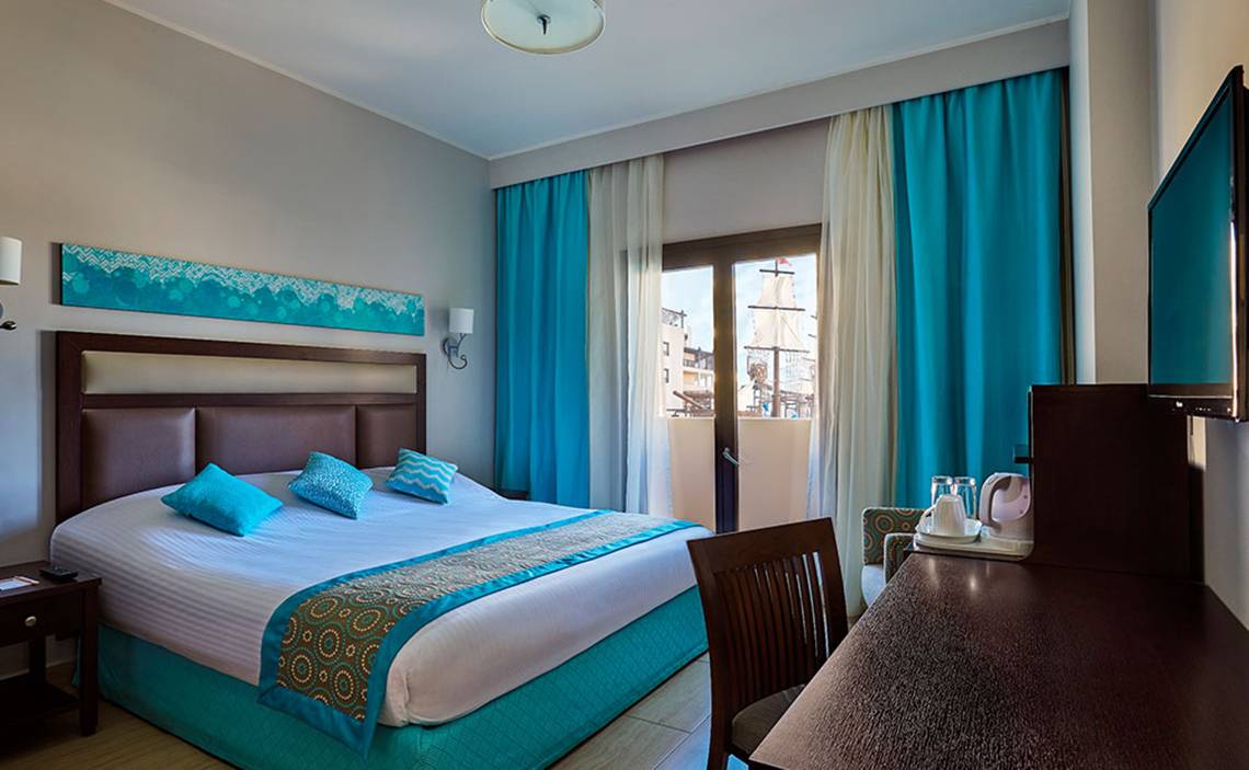 Hotelzimmer im Steigenberger Aqua Magic mit blauen Vorhängen, Doppelbett und Schreibtisch.