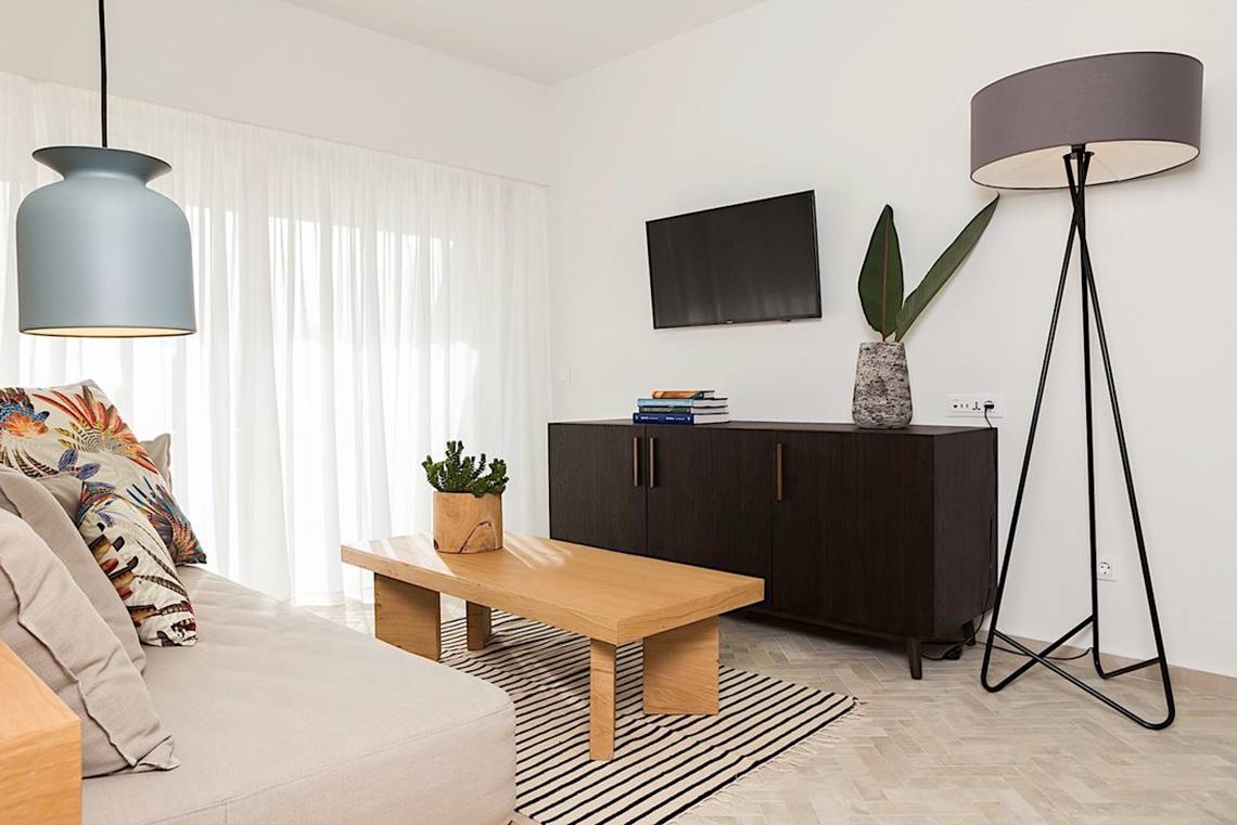 Ein Wohnzimmer mit Fernseher, Tisch, Lampe und Sofa im Cretan Malia Park Hotel.