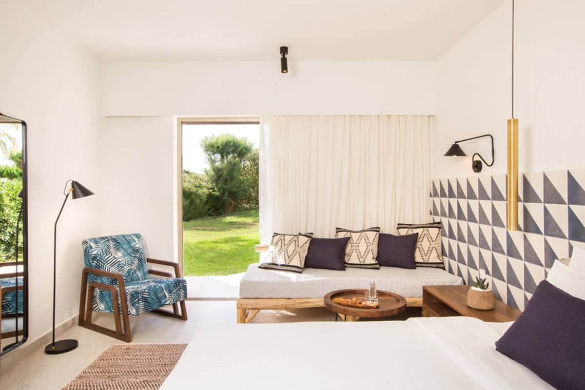 Innenansicht eines Zimmers im Cretan Malia Park Hotel mit weißem Bett, Sofa, Tisch und Dekoration.
