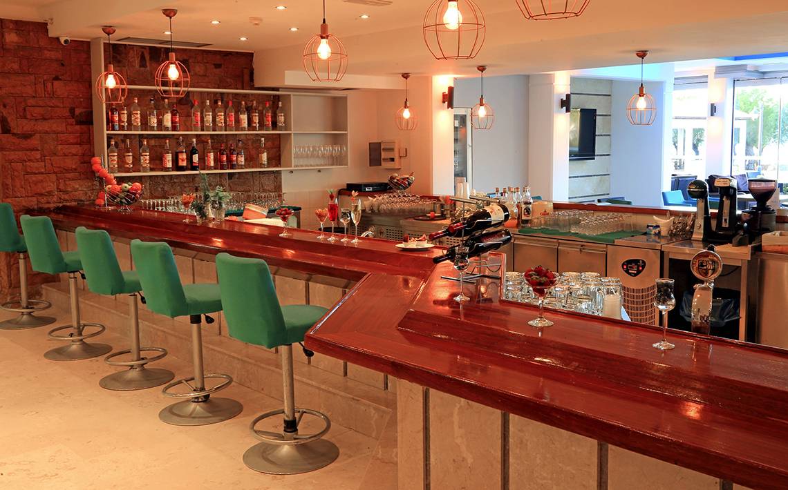 Bar im Blue Bay Beach Resort Hotel mit grünen Stühlen und einer Theke.