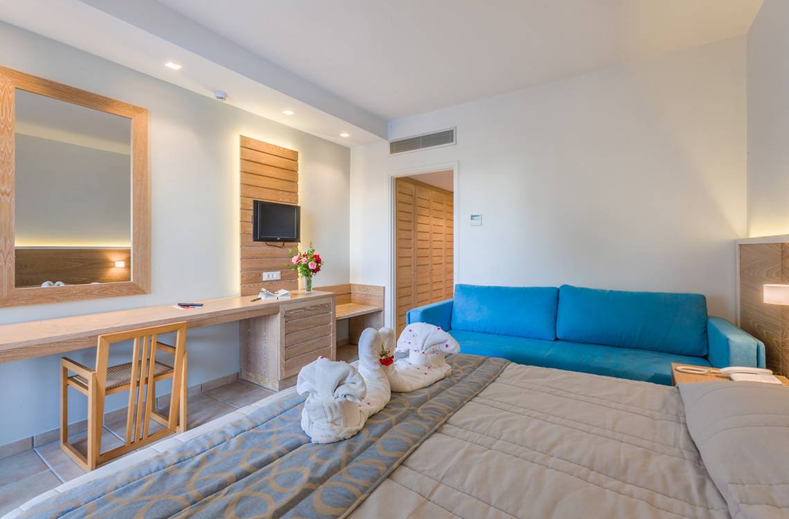 Zimmer im Tigaki Beach Hotel mit Bett, Couch, Schreibtisch und Fernseher