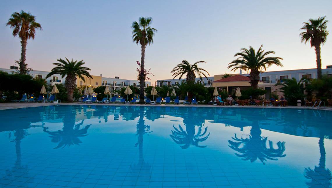 Ein Swimmingpool im Tigaki Beach Hotel mit blauem Wasser und reflektierenden Palmen.