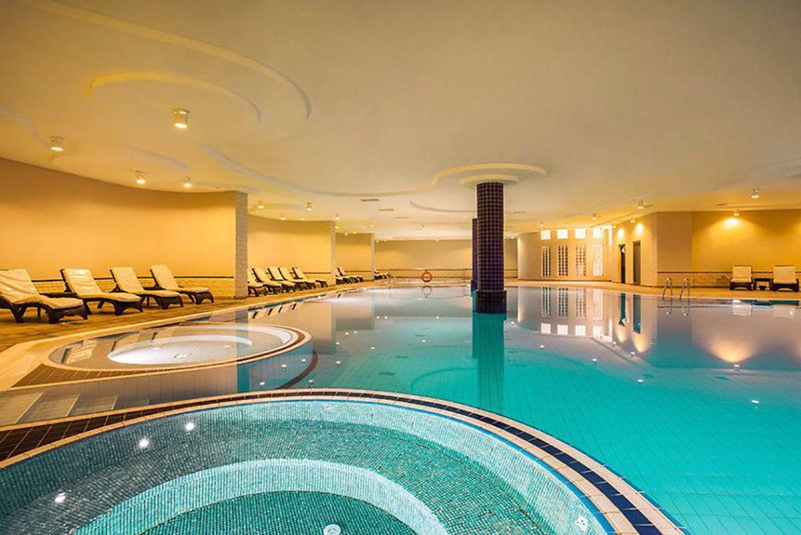 Schwimmbecken im Turan Prince Hotel mit Liegestühlen und gelben Wänden.