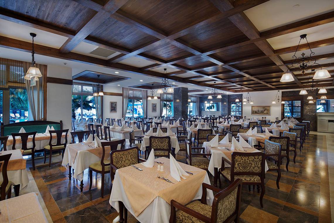 Innenansicht des Restaurants im Alba Queen Hotel mit vielen gedeckten Tischen und Holzdecken.