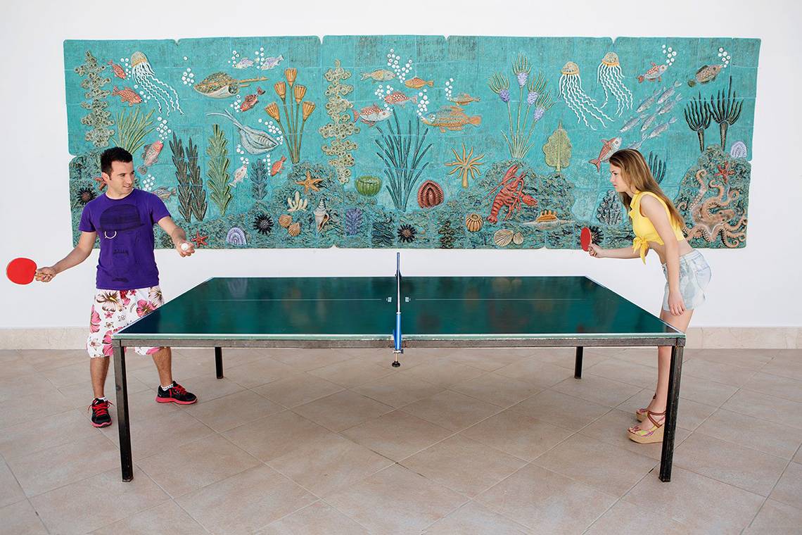 Ein Paar spielt Tischtennis vor einer Wand mit einem Wandteppich, der Meeresleben darstellt.