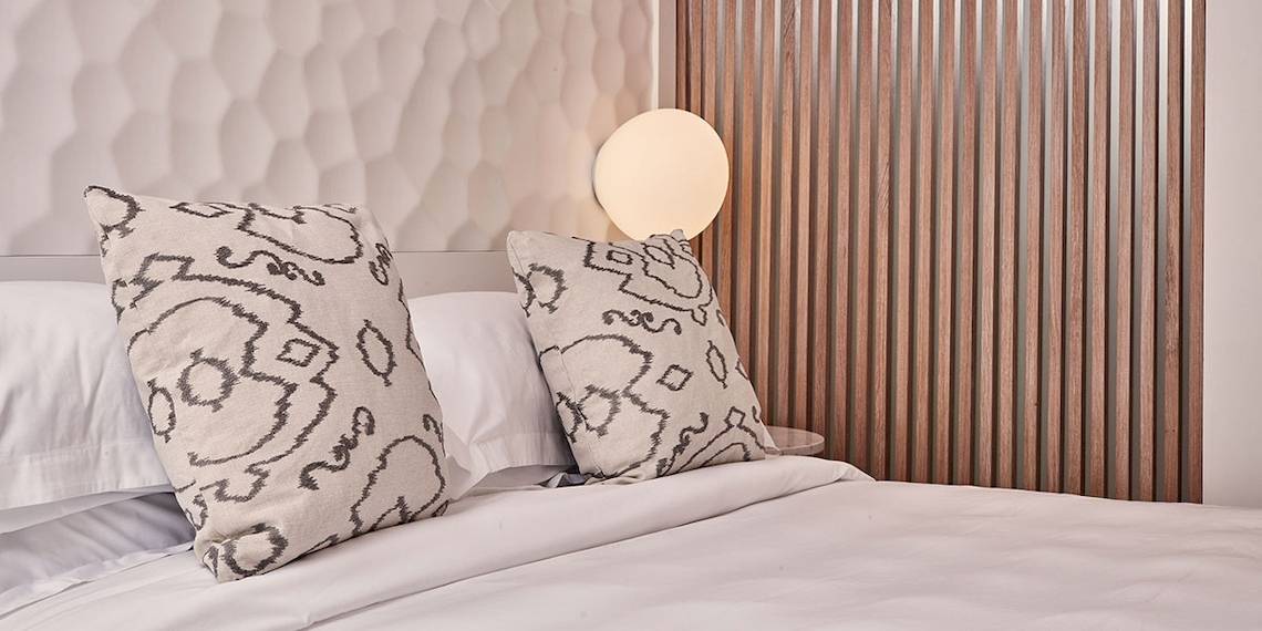 Bett im Myconian Kyma Hotel mit weißen Laken und gemusterten Kissen.