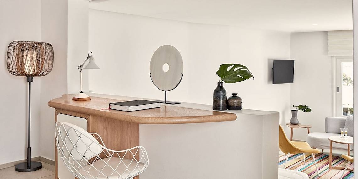 Innenbereich des Myconian Kyma Hotels mit heller Wand, Schreibtisch, Lampe, Dekor und Pflanzen.