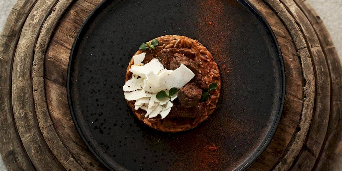 Ein Gericht auf einer schwarzen Holzplatte im Myconian Kyma Hotel, bestehend aus Fleischbällchen, Risotto und Käse.