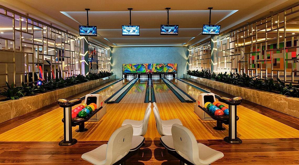 Innenansicht der Bowlingbahn im Regnum Carya Golf & Spa Resort mit bunten Wänden und Fernsehern an der Decke.