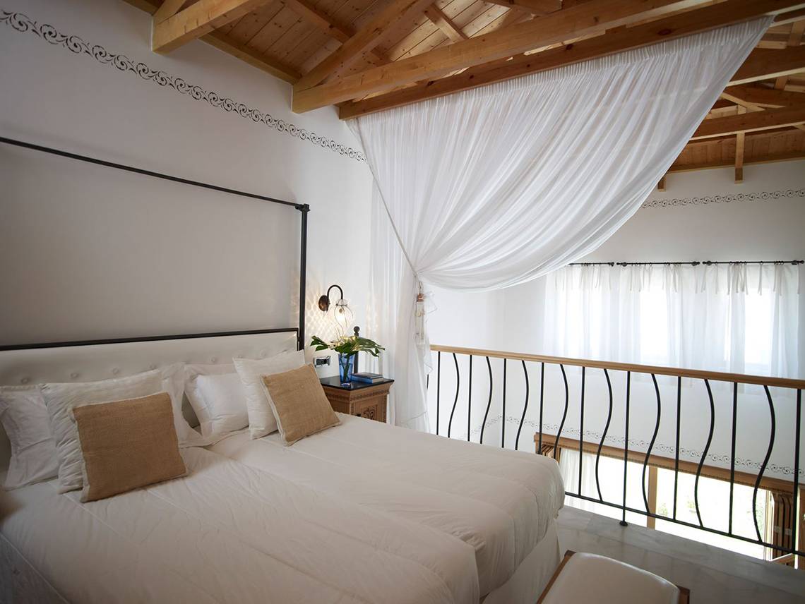 Schlafzimmer im Mitsis Blue Domes Resort mit weißem Bett, Kissen, und einem Balkon mit Geländer.