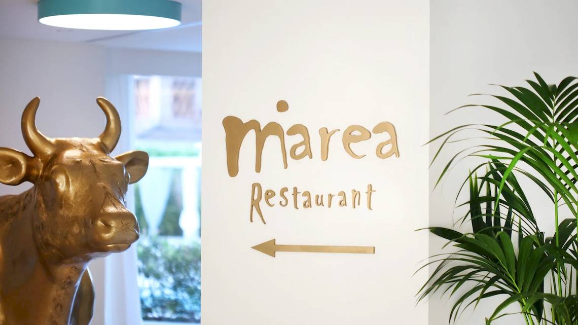 Eingang zum Marea Restaurant mit goldener Kuh Statue und grüner Pflanze.