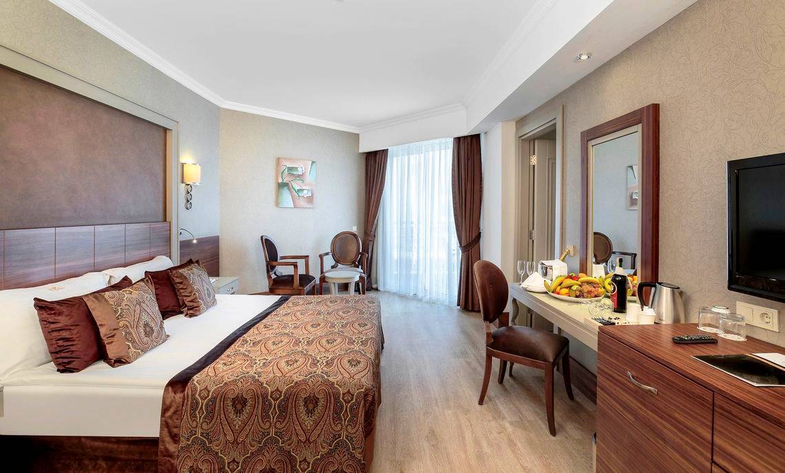 Innenansicht eines Zimmers im Well Palace Side Hotel mit Bett, Schreibtisch und Früchten.