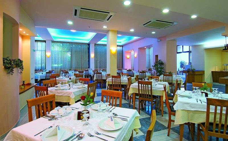 Innenansicht des Restaurants im Eva Bay Hotel mit gedeckten Tischen und farbiger Beleuchtung.