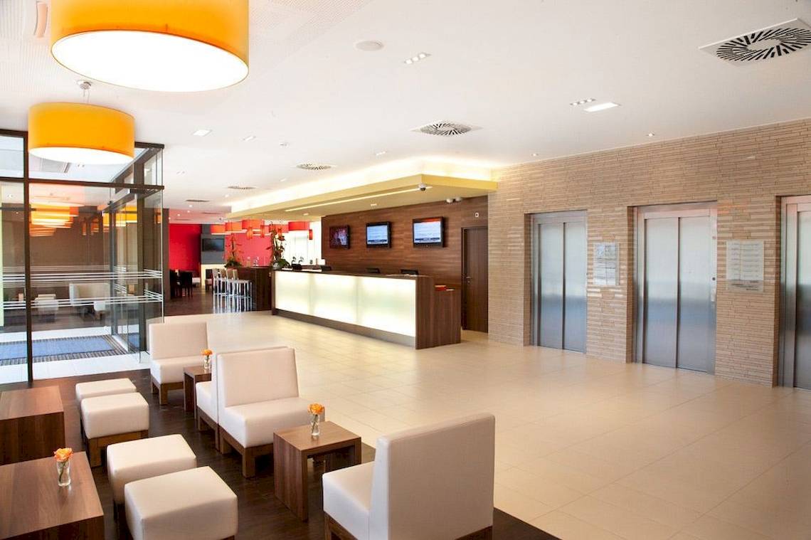 Lobby des Star Inn Hotel Wien Schönbrunn mit Rezeption, Sitzbereichen und Aufzügen.