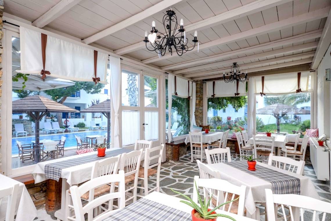 Innenbereich des Alkyoni Beach Hotels mit Tischen, Stühlen und Aussicht auf den Pool.