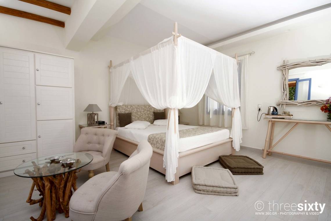 Schlafzimmer im Alkyoni Beach Hotel mit Baldachinbett, zwei Sesseln, Glastisch und Dekor.