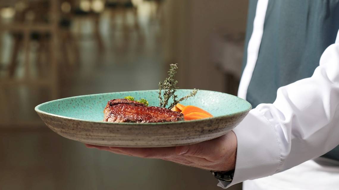 Ein Kellner hält eine Platte mit einem gebratenen Gericht und Beilagen im Iberostar Selection Sabila Hotel.