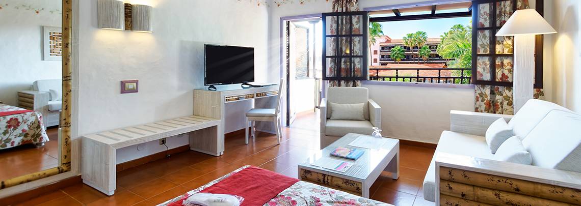 Innenansicht eines Hotelzimmers mit Schreibtisch, Fernseher, Bett, Sofa und Balkon mit Ausblick.