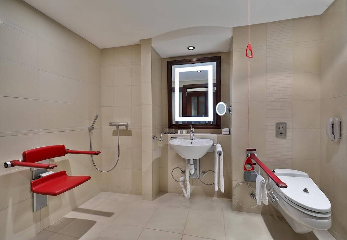 Barrierefreies Badezimmer im Sheraton Oman mit einer roten Sitzbank und einem behindertengerechten WC.