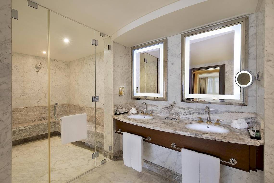 Badezimmer im Sheraton Oman mit Marmorboden, Regendusche und Doppelwaschbecken.