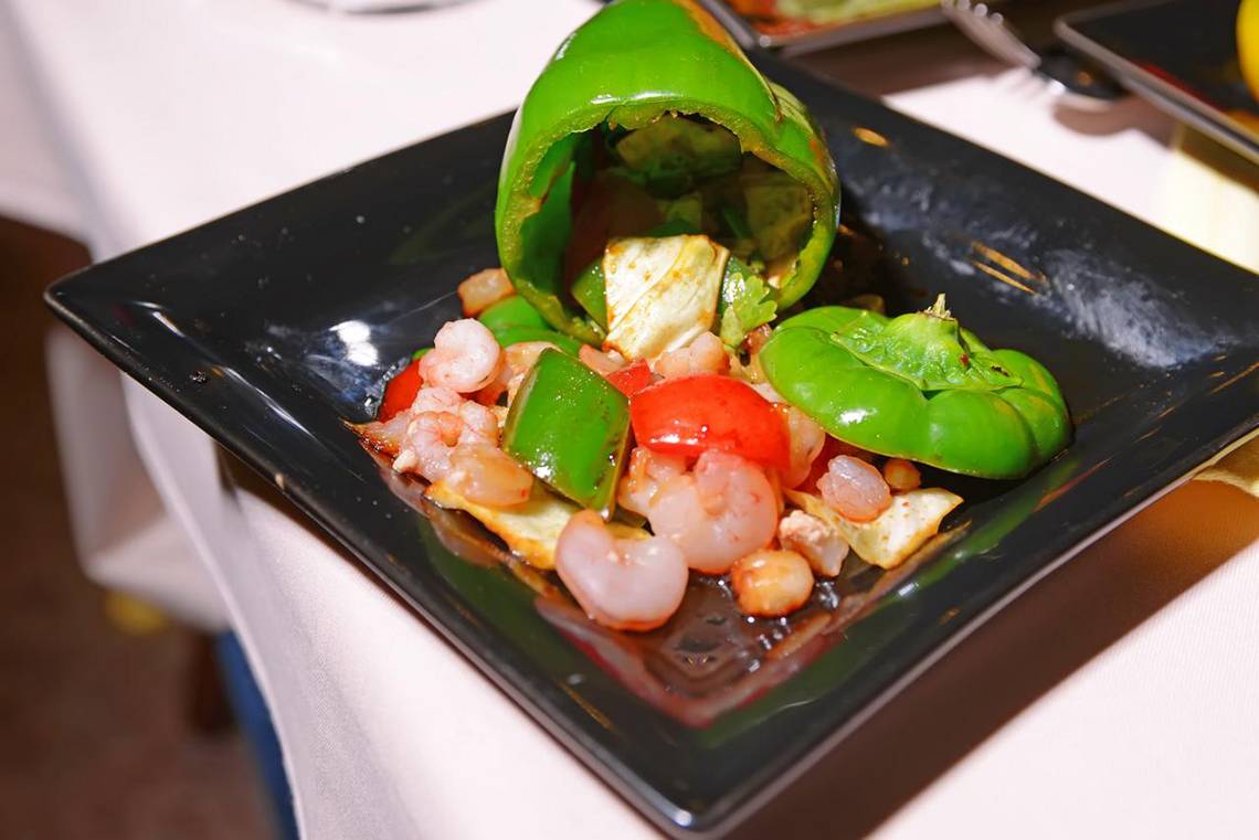 Gerecht mit Garnelen und gefüllten Paprika auf schwarzem Teller.